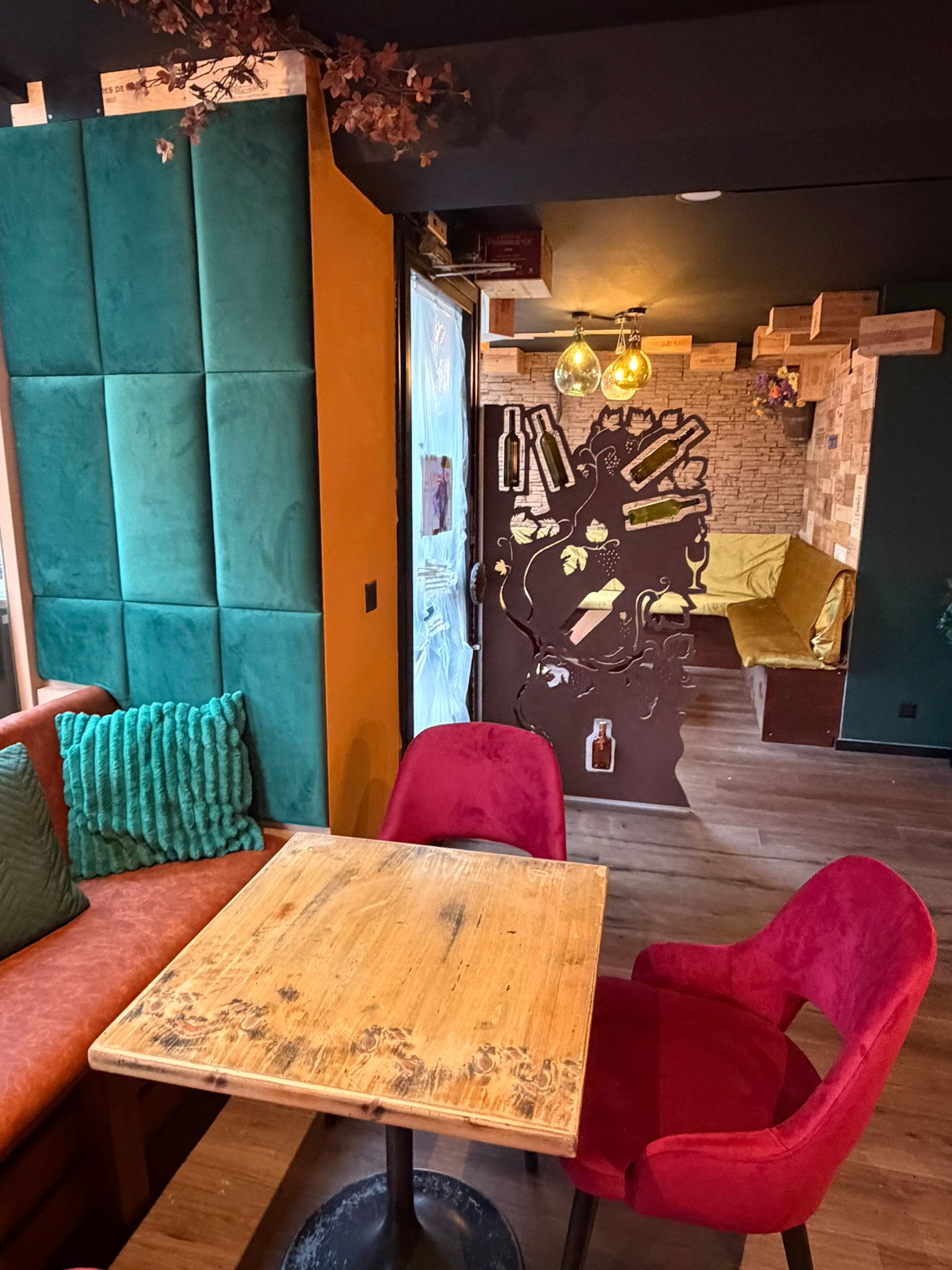 Coin lounge d'Origen Riviera avec panneaux bleu-vert, table en bois et fauteuils rouges.