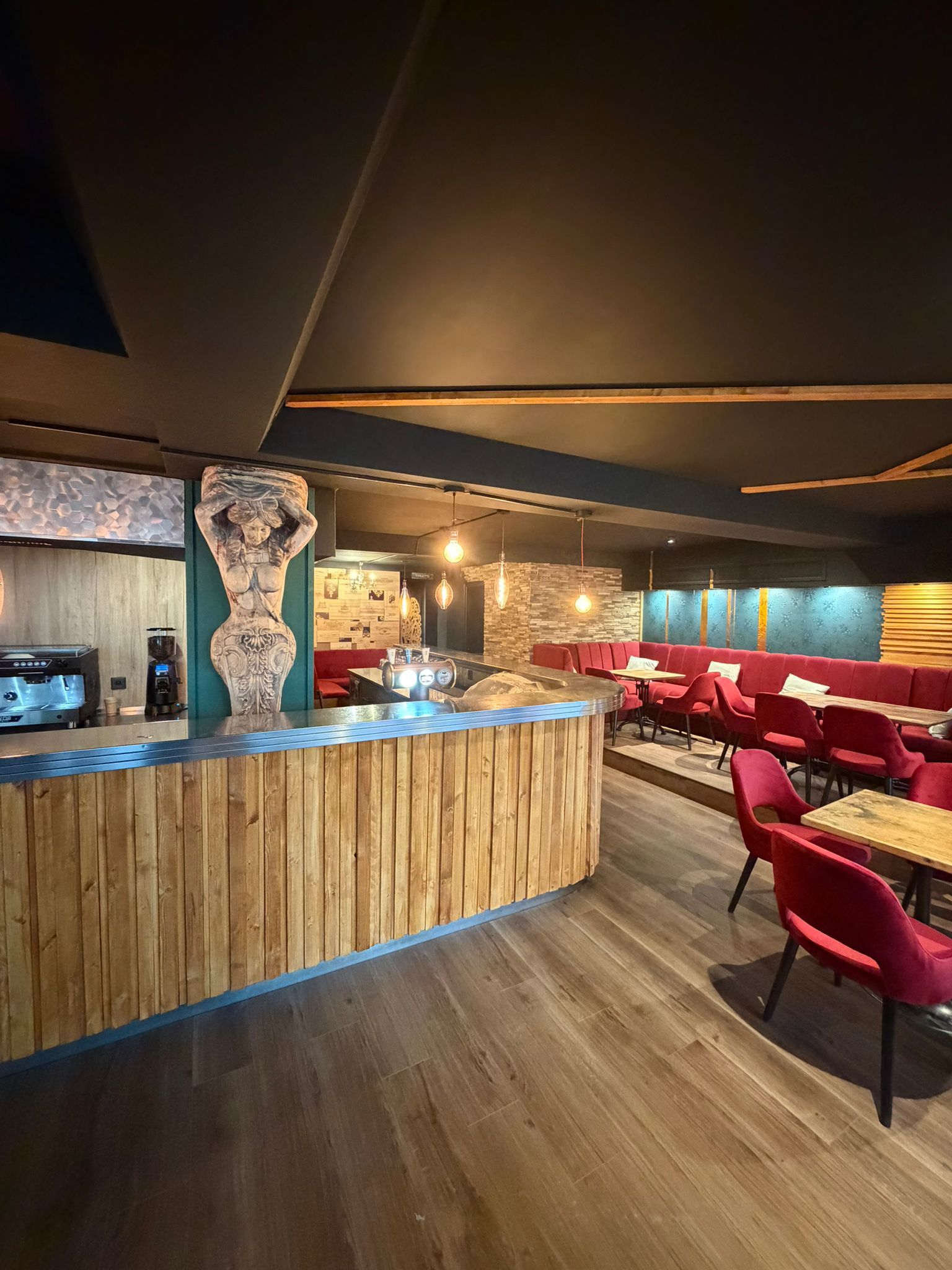 Comptoir en bois d'Origen Riviera avec banquettes rouges, tables et suspensions lumineuses.